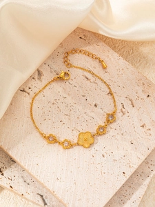 Macro detail of gold titanium flower and star charms bracelet on silk fabric