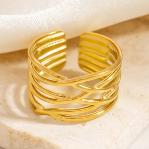 Detail of multi-layer layered hollow gold ring on white silk and stone surface
