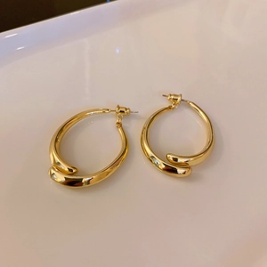 Detailed shot of polished gold irregular twisted hoop earrings on a neutral tray