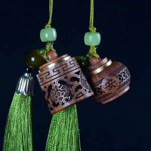 Detailed view of carved sandalwood pendant with green tassels and peace symbol