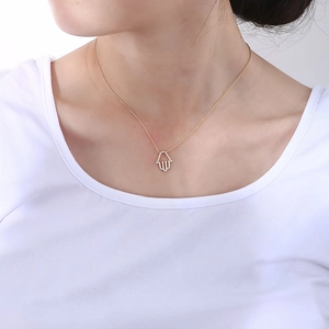 Gold Hamsa Hand necklace with white zircons worn by a model on a white shirt