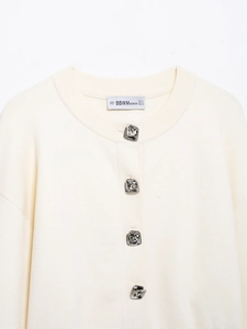 Detail view of irregular silver flower buttons on a creamy white knit cardigan