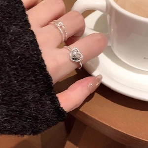 Silver stackable heart and rope rings worn by a model in a cozy, elegant lifestyle setting