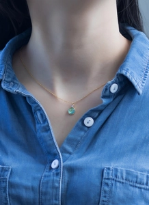 Detailed view of a gold chain necklace with a round teal pendant on a model wearing denim