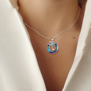 Detail view of a silver necklace with blue-purple crystal pendant on a model neckline