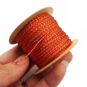 Close-up of 1mm red and gold twisted cord roll held by hand for DIY jewelry making
