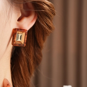Close-up of rectangular amber resin earring with gold-tone setting on model's ear