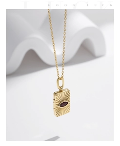 Close-up of gold square pendant with sunburst texture and red gemstone inlay