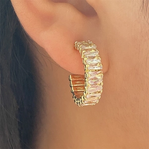 Gros plan de boucles d'oreilles dorées en C avec zircons carrés portées par un mannequin