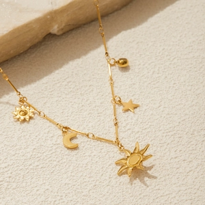 Dettaglio ravvicinato dei ciondoli sole luna e stella in oro 18K su collana d'acciaio