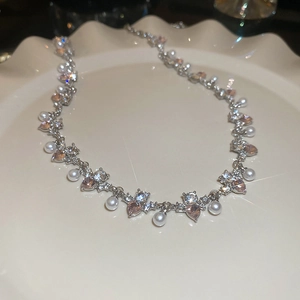 Close-up of heart-shaped pink crystals and pearls on a silver necklace in a ceramic dish