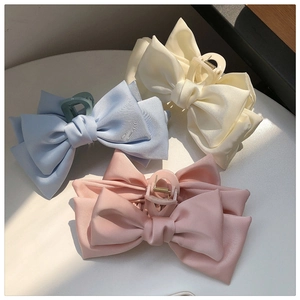 Three oversized fabric bow hair clips in cream, light blue, and pink on a white table