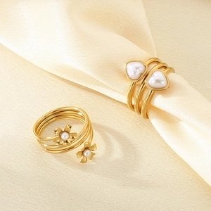 Detailed shot of 18k gold plated flower and heart pearl rings on beige silk fabric