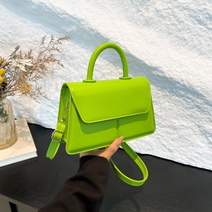 Minimalist green crossbody bag with top handle and strap shown against white wall
