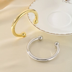 Minimalist C-shaped open gold and silver bangles displayed on luxury champagne silk fabric