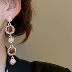 Close-up of gold fringe earrings with layered pearls and brown tiger eye stones on model