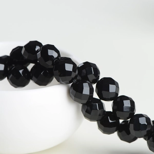 Faceted natural black onyx gemstone beads for DIY jewelry making displayed on a white bowl