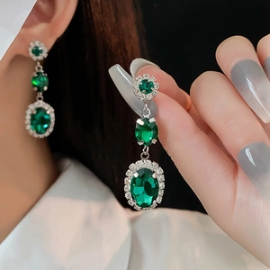 Close-up of green emerald-cut drop earrings with silver diamond halo on model