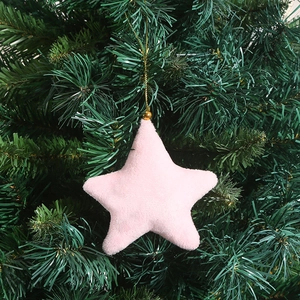 Pink star-shaped plush Christmas ornament hanging on a green tree with gold cord