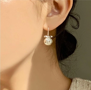 Detail of silver bow and round white pearl earring worn on ear with soft lighting