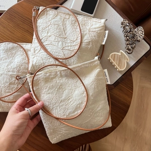 Detail of floral embroidery on linen crossbody phone bag with brown leather strap