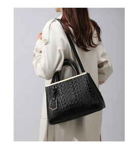 Close-up of black crocodile pattern shoulder bag with gold hardware worn by model