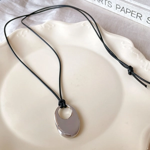 Minimalist silver oval hollow pendant necklace with sleek black cord on a ceramic plate