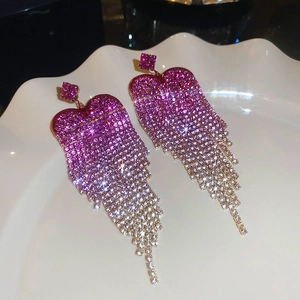 Close-up of heart-shaped tassel earrings with gradient rhinestones on a white plate