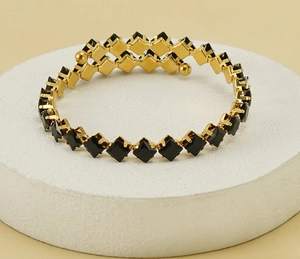 Detail of gold spiral bracelet featuring square black crystals and gold spherical ends