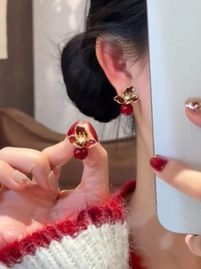Gros plan de boucles d'oreilles fleurs rouges aux bords dorés portées à l'oreille