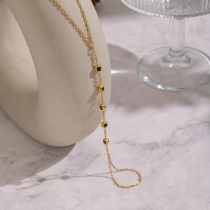 Dettaglio di una collana dorata con pietre verde oliva su uno sfondo di marmo bianco
