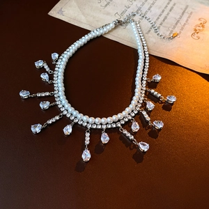 Détail d'un collier double couche avec perles blanches, strass et gouttes de zircone