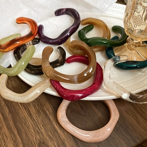 Close-up of irregular resin bangles in amber, burgundy and olive on a white ceramic plate
