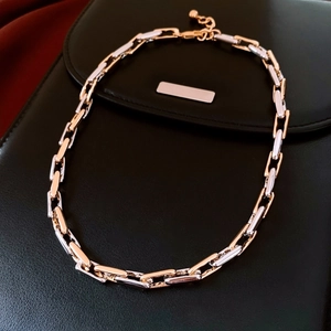 Detail view of two-tone gold and silver alloy chain necklace on black leather bag