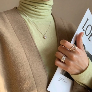 Close-up of a minimalist silver heart pendant necklace and irregular thick band rings