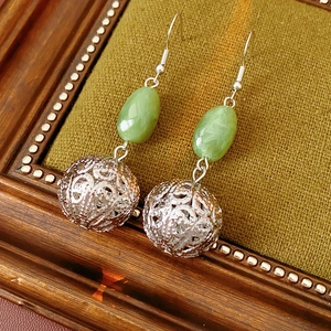 Detail of hollow silver metal sphere and green oval resin bead earrings on vintage wood