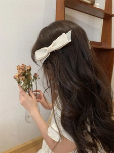 Eleganter weißer Satin-Schleifen-Haarclip an einem Modell mit langen Locken