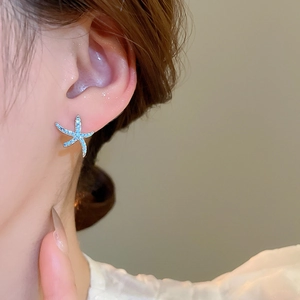 Primo piano di un orecchino a lobo a stella marina blu con zirconi indossato da modella
