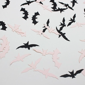 Halloween party confetti with black and light pink paper bat shapes on white background