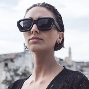Chic women's chunky black rectangular sunglasses worn by a fashion model with gold earrings