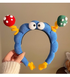 Dettaglio del cerchietto blu in peluche a forma di mostro con decori colorati