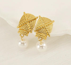 Close-up of golden woven texture metal stud earrings with elegant white pearl drops