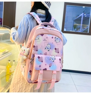 Pink cartoon backpack with plush bear pendant shown on model in a bright setting