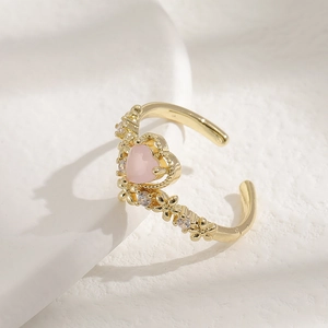 Adjustable pink heart ring with gold finish and floral accents on a white display