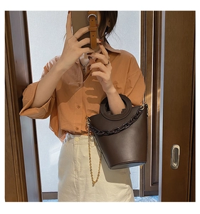 Deep brown bucket bag with thick chain detail and round handle on a shoulder model