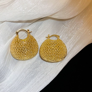 Macro detail of vintage gold oval basket earrings with intricate hollow woven metal texture