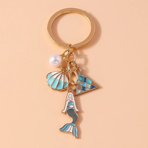 Detail of mermaid and seashell pendants on a gold keychain with blue shell and white pearl