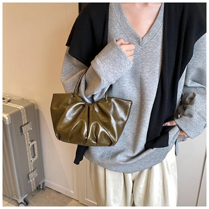 Detail of the olive green pleated cloud bag shown held by a model in a natural setting