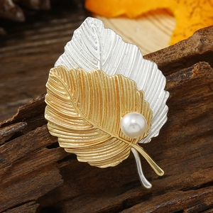 Detailed view of dual-tone gold and silver leaf brooch with a pearl on rustic wood