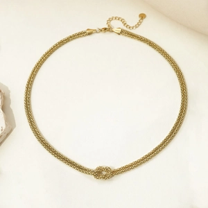 Dettaglio di una collana dorata con pendente a nodo e catena intrecciata su pietra